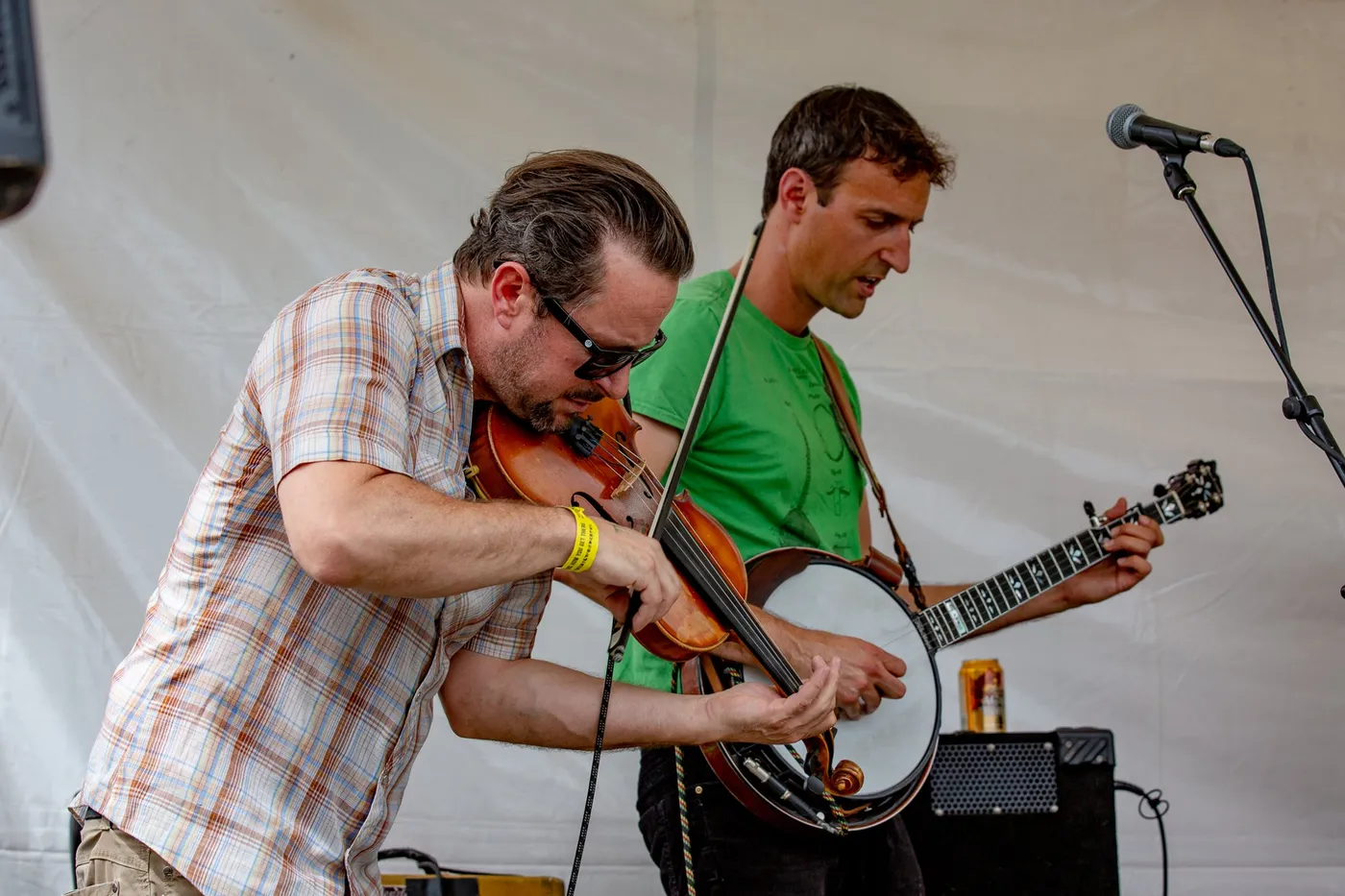 A banjo player in a plaid shirt picking hard under a white stage tent
