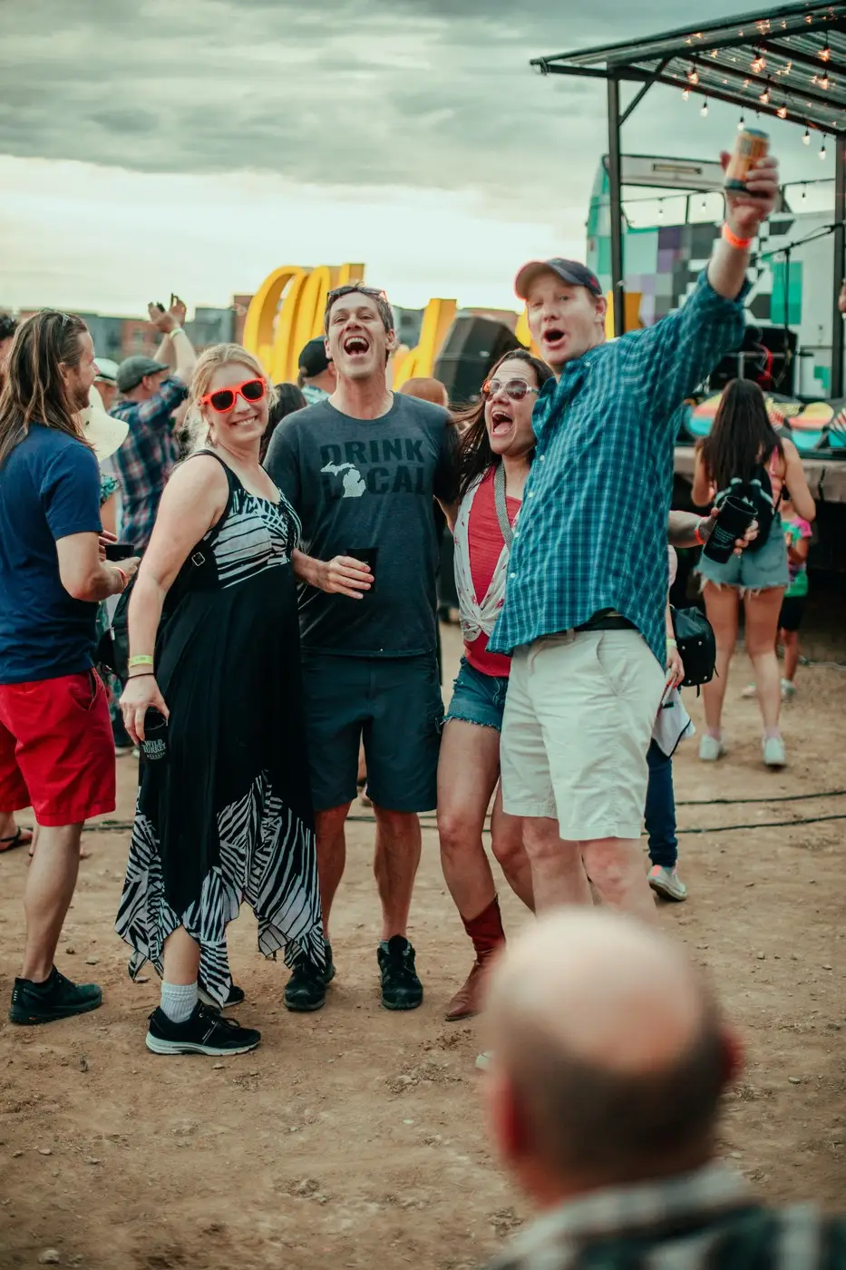 Four friends in sunglasses with their arms up, shouting along to the band.
