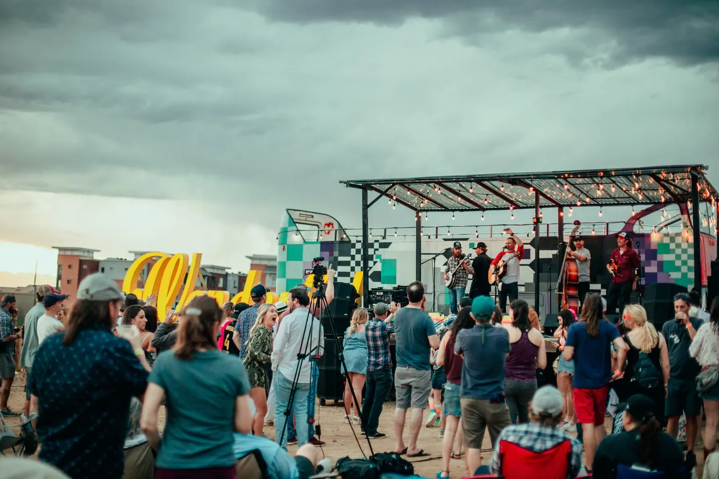 The crowd in front of the stage with the yellow script sign lit behind the band.