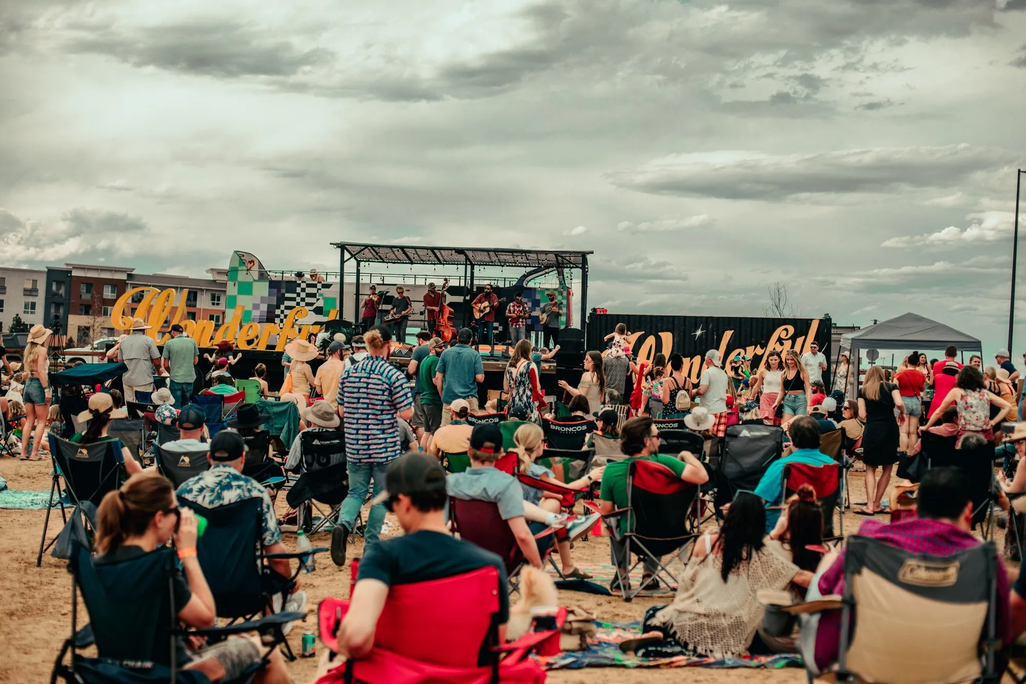A packed crowd facing the stage under a wide Colorado sky, hands up