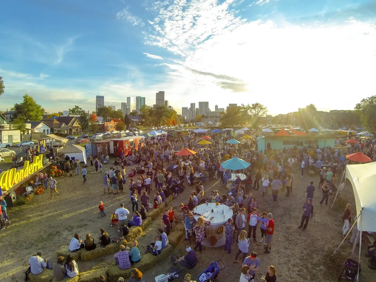 Tents and a festival crowd from above at golden hour, the Denver skyline on the horizon