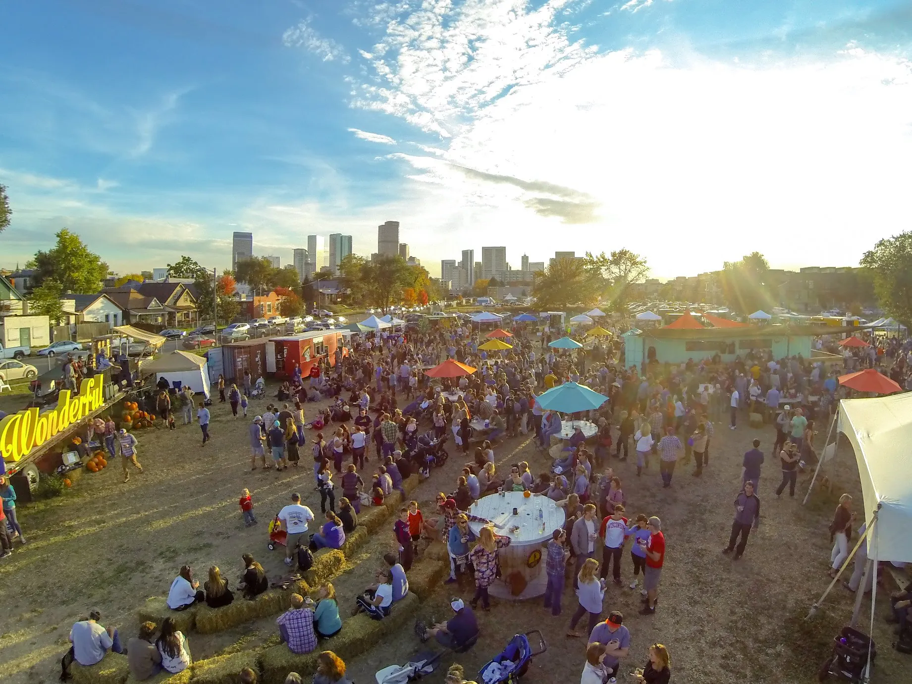 Tents and a festival crowd from above at golden hour, the Denver skyline on the horizon