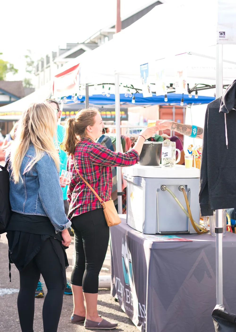 A shopper in a flannel shirt browsing a maker's booth of clothing and jewelry under a tent