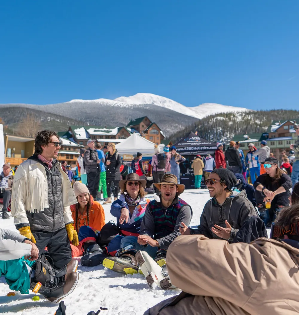 Festival crowd on the snow at the Winter Park Resort base area, ski runs and peaks behind them