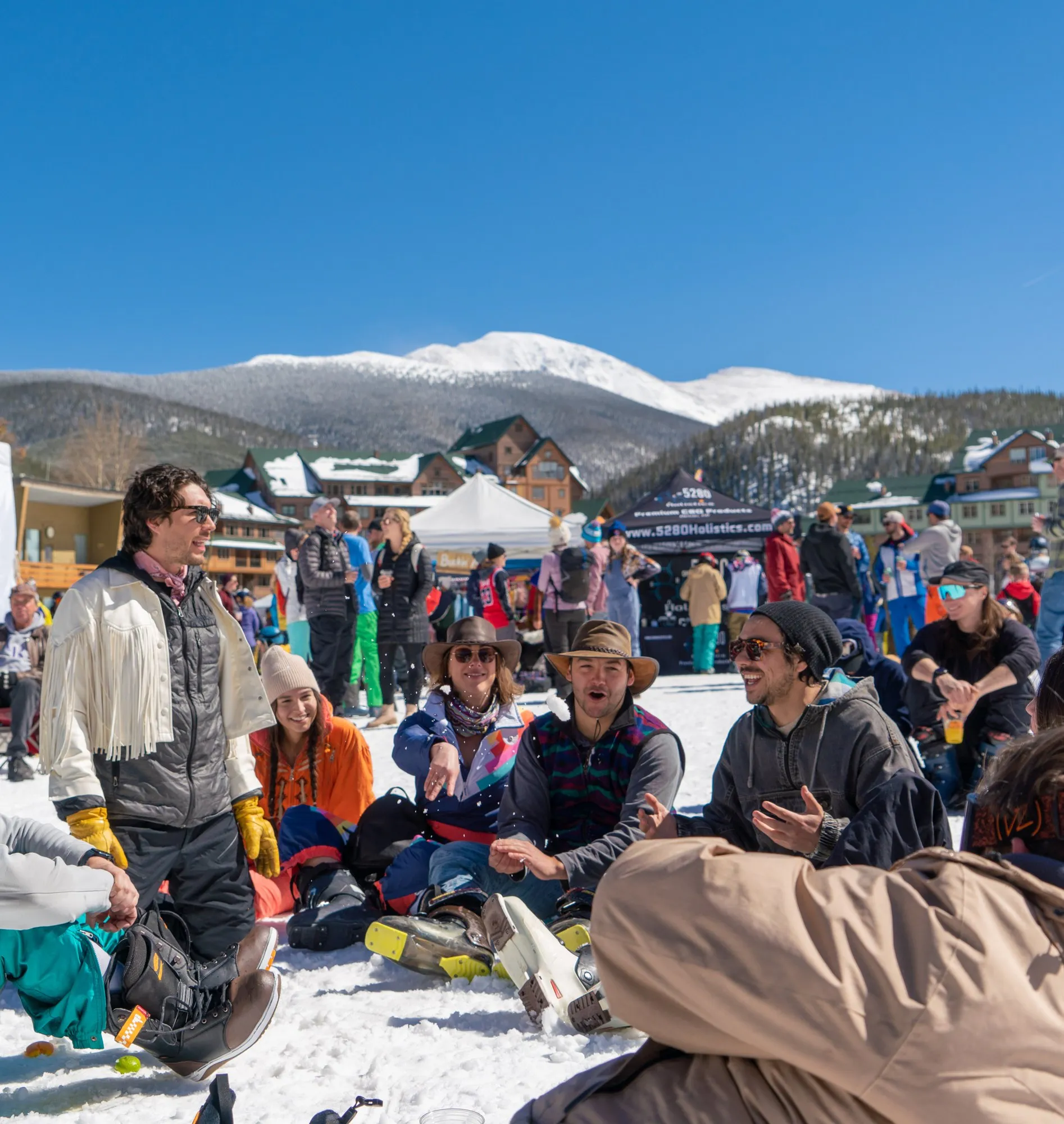Festival crowd on the snow at the Winter Park Resort base area, ski runs and peaks behind them