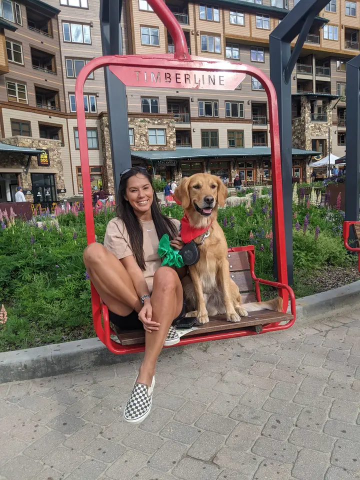 A woman and her dog sitting in a red chairlift frame.