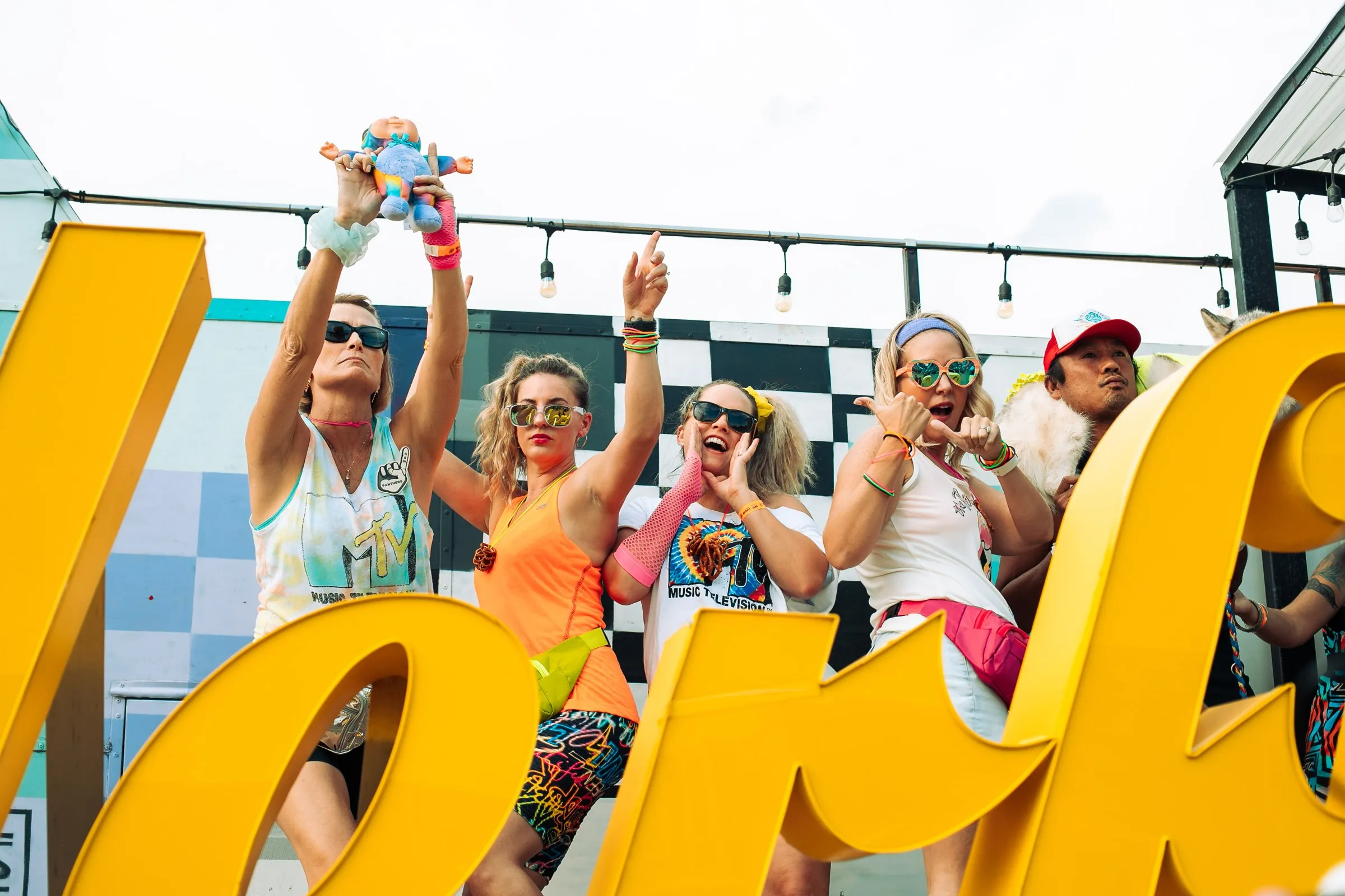 A row of friends in 80s tank tops, sweatbands and sunglasses dancing on the stage behind the Wonderful sign