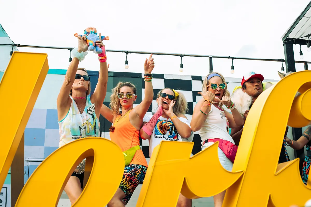A row of friends in 80s tank tops, sweatbands and sunglasses dancing on the stage behind the Wonderful sign