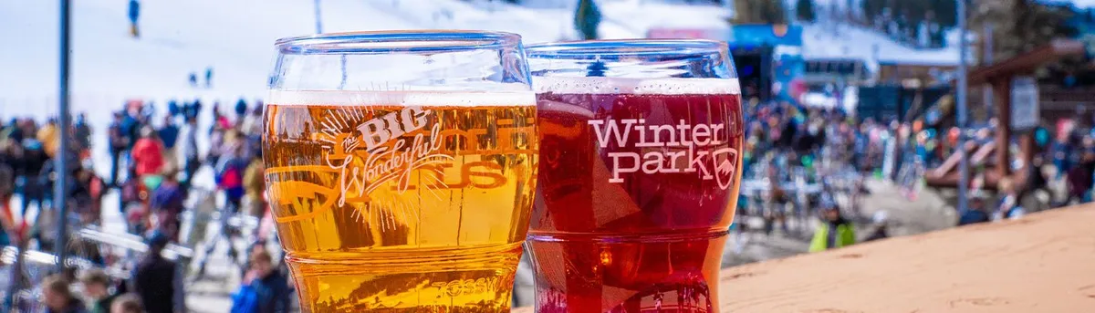 A tasting glass raised over the crowd on the snow at the Winter Park Resort base area, the stage and the peaks behind