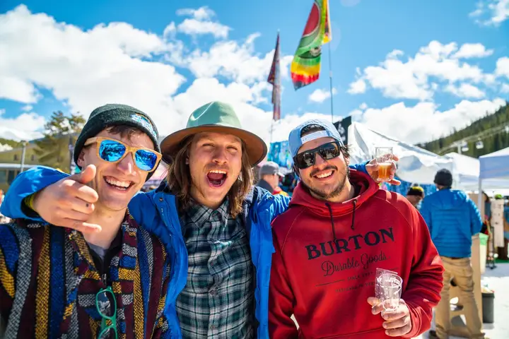 Three friends in ski jackets and sunglasses cheering with their tasting cups.
