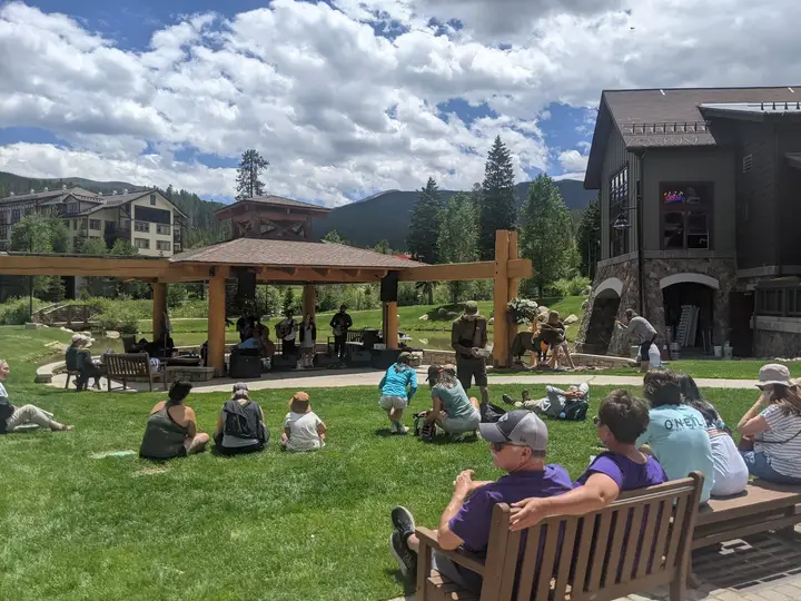 People on the lawn in the sun with the lodge and the mountains behind.
