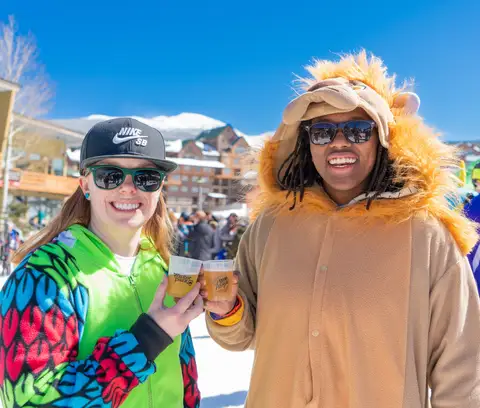 A couple in a tie-dye onesie and a lion onesie holding beers.