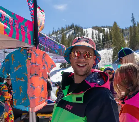 A man in a bucket hat and neon jacket laughing.