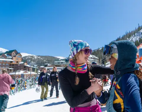 Two friends in goggles with arms spread wide.