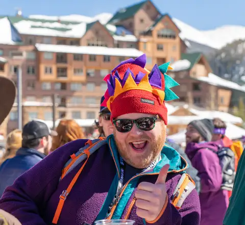 A man in a jester hat and sunglasses laughing.